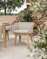 Outdoor rattan dining chair with light cushion and wooden legs on tiled patio