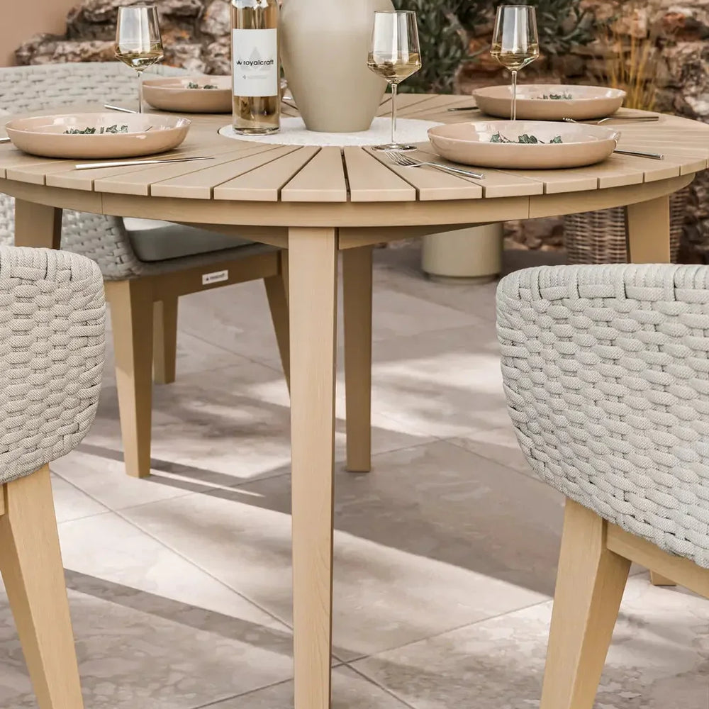 Round wooden outdoor dining table with beige rope chairs set for four on patio tiles