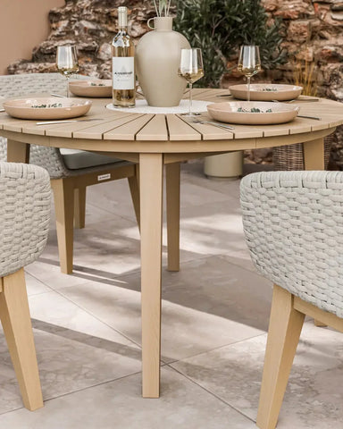 Round wooden outdoor dining table with beige rope chairs set for four on patio tiles