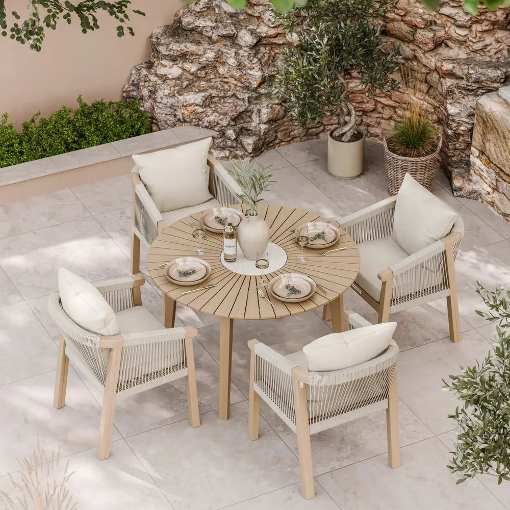 Round wooden outdoor dining table with four rope armchairs and cream cushions on patio