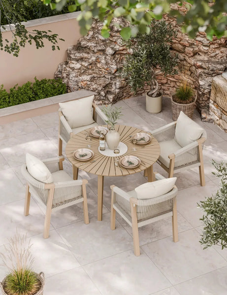Round wooden outdoor dining table with four rope armchairs and cream cushions on patio