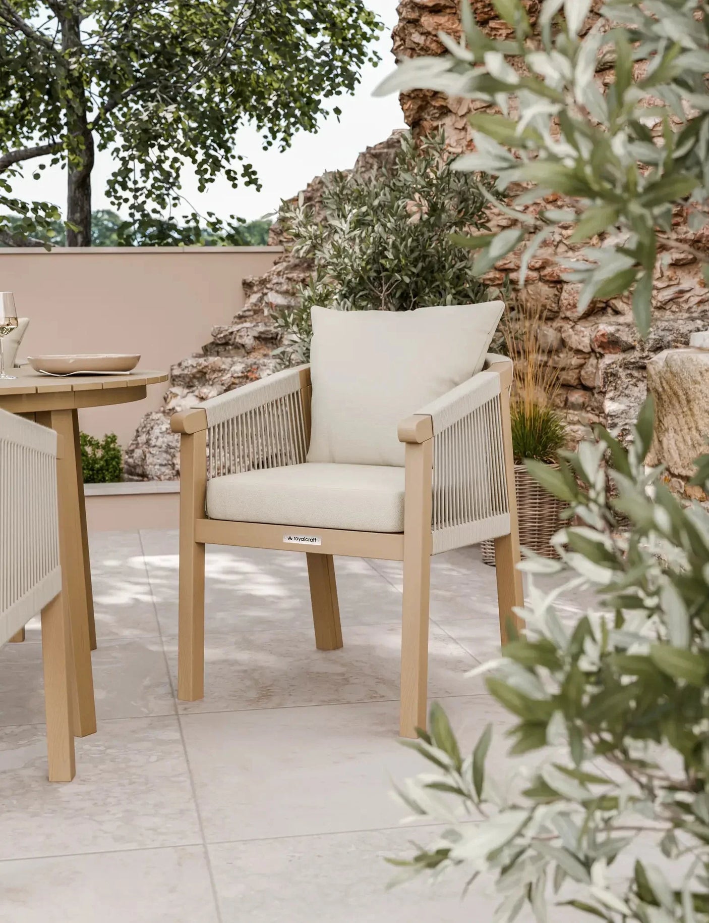 Outdoor rope dining chair with beige cushions on a tiled patio near a stone wall and plants