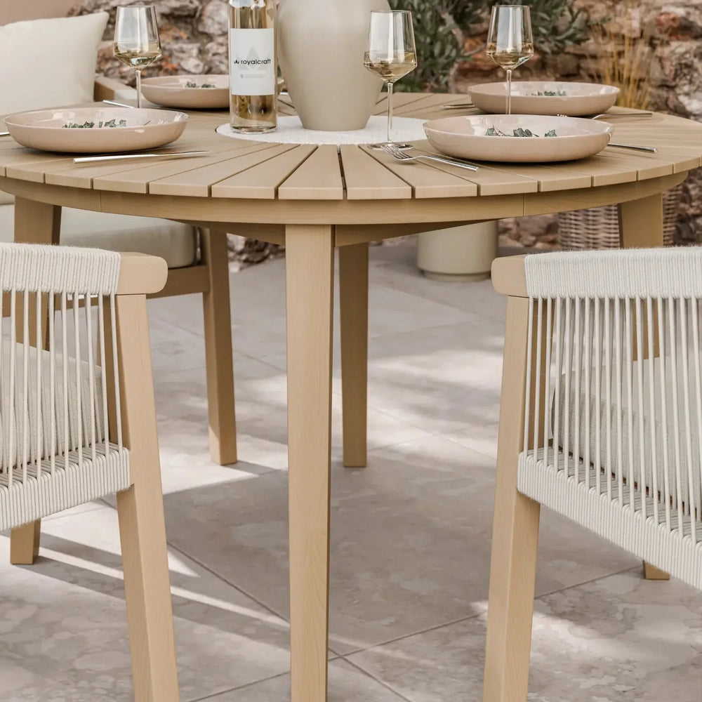 Round wooden dining table with beige rope chairs set for four on patio tiles