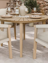 Round wooden dining table with beige rope chairs set for four on patio tiles