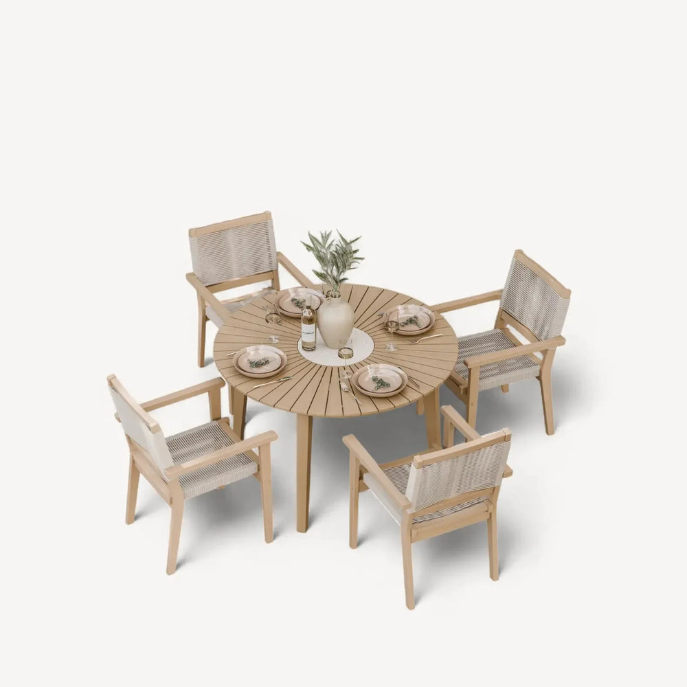 Round wooden dining table set with four woven chairs and tableware arranged on top