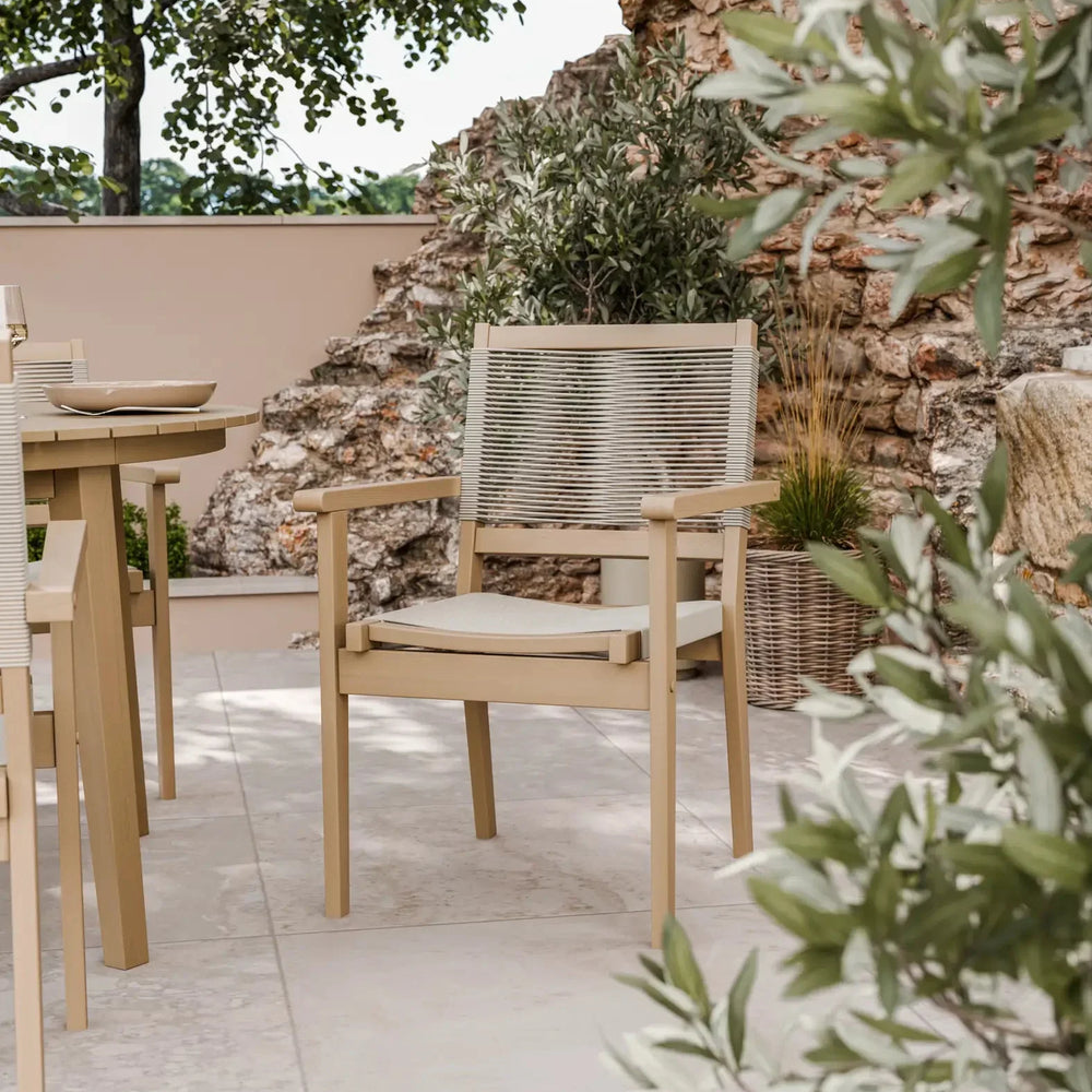 Beige outdoor dining chair with woven rope backrest and seat cushion on stone patio