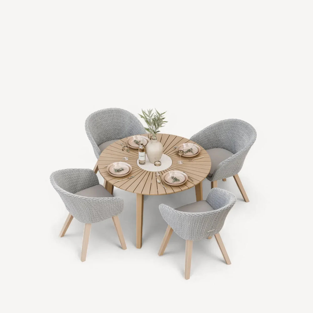 Round wooden dining table with four grey woven chairs set for a meal