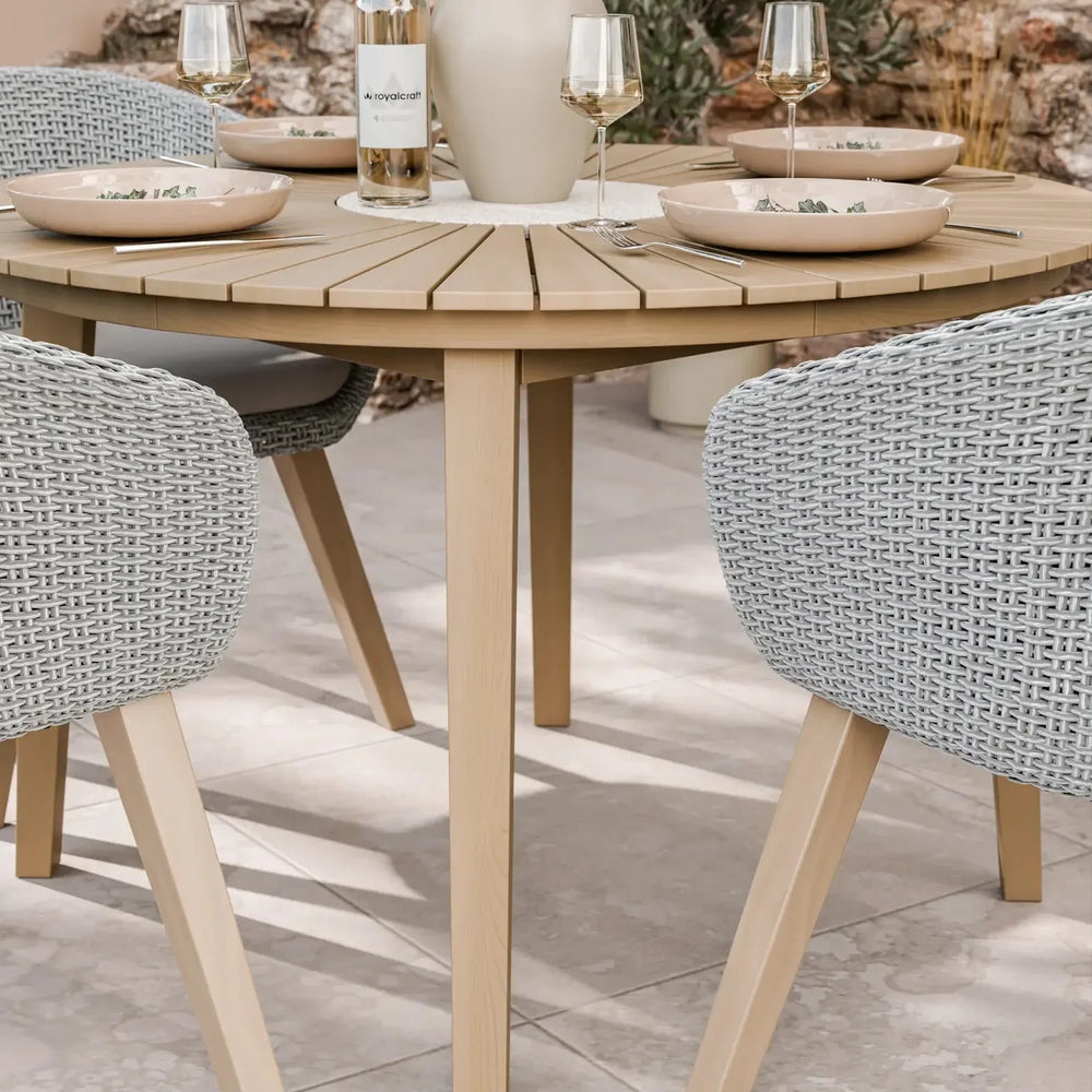 Round wooden outdoor dining table with wicker chairs, set for four with plates and glasses