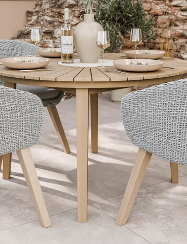 Round wooden outdoor dining table with wicker chairs, set for four with plates and glasses