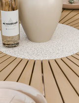Round slatted wood dining table with speckled stone centrepiece and beige vase