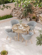 Round patio dining table with wood slats and four grey woven garden chairs on stone tiles