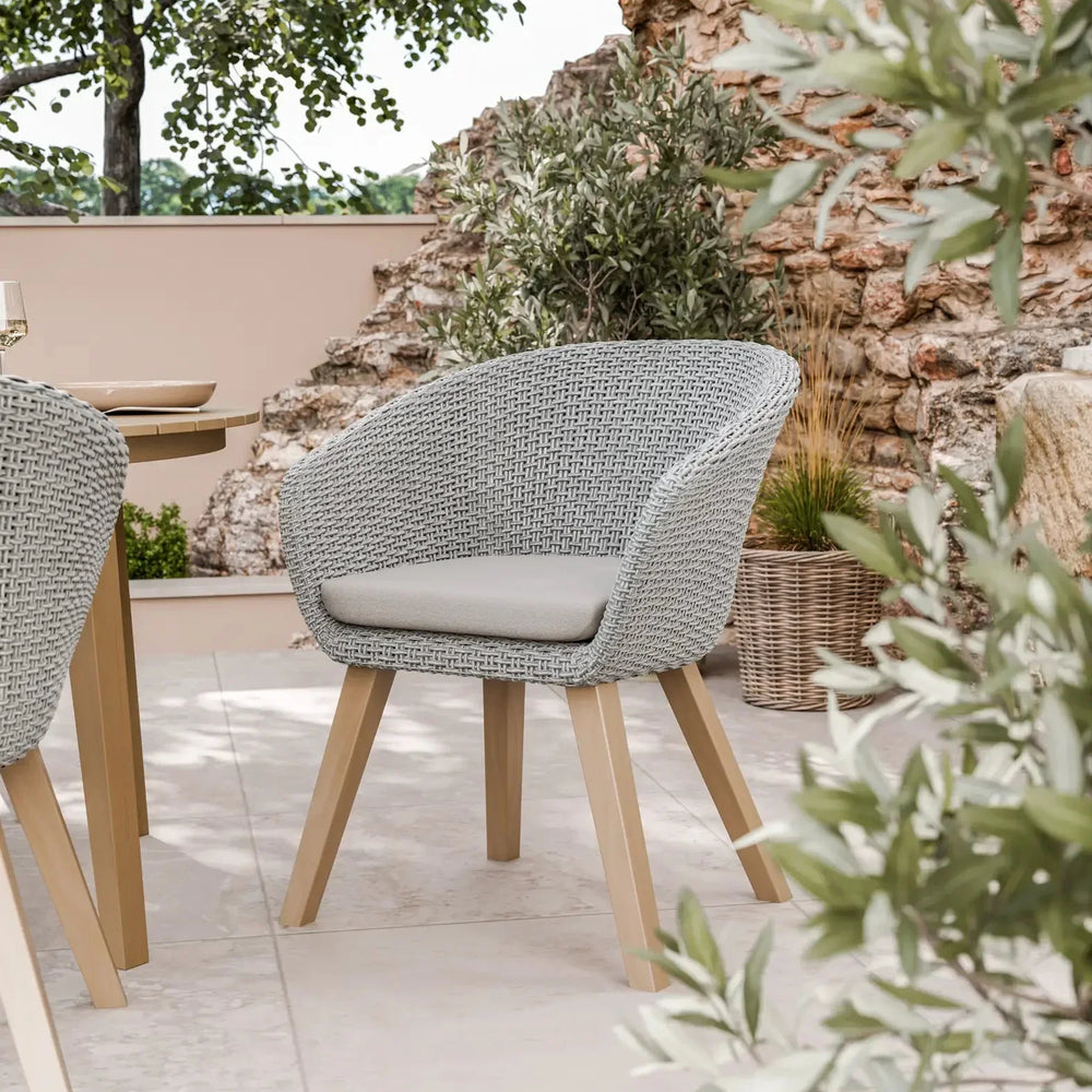 Grey rattan outdoor dining chair with cushion and wooden legs on stone patio