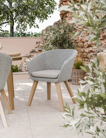 Grey rattan outdoor dining chair with cushion and wooden legs on stone patio