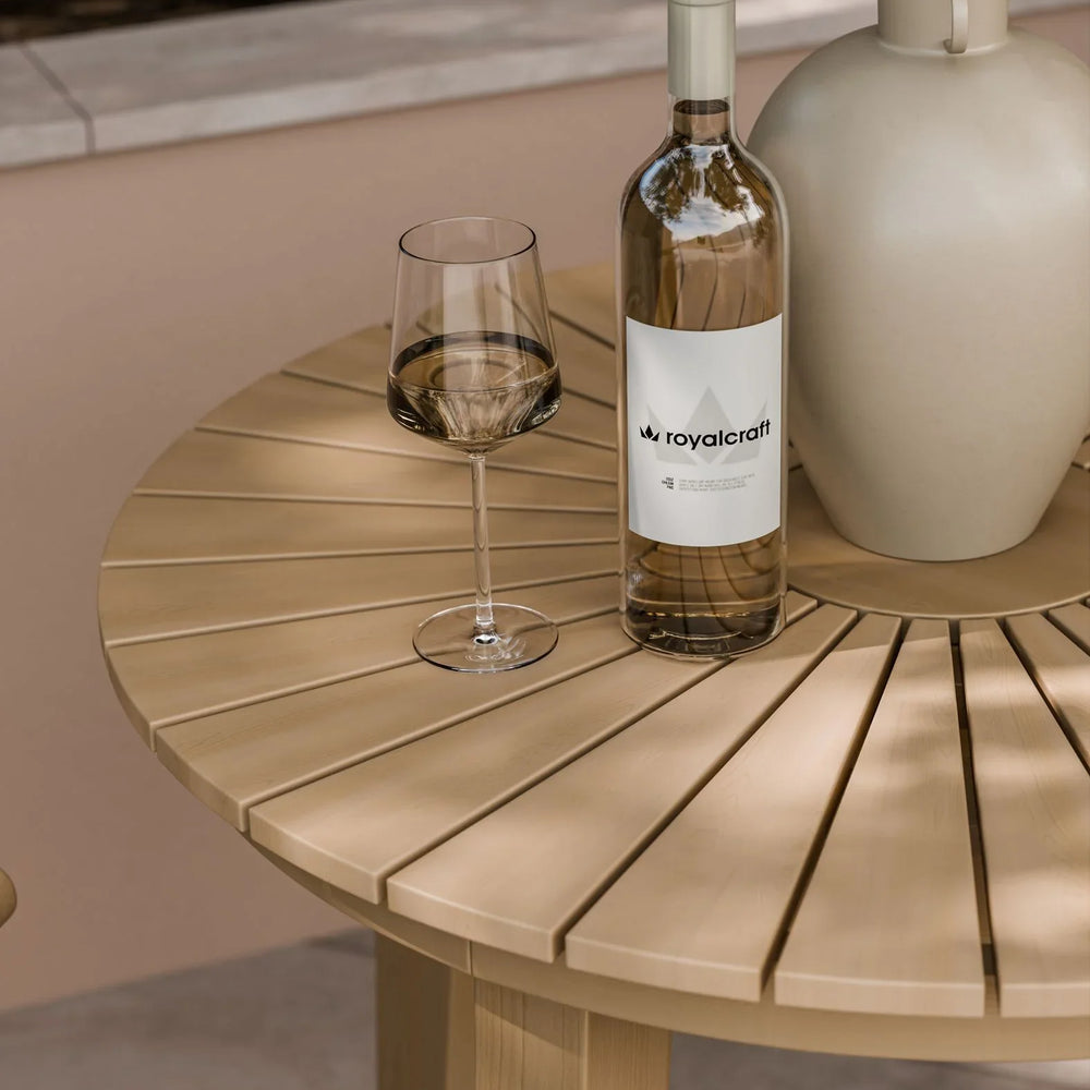Round natural wood outdoor dining table with wine bottle, glass, and decorative vase