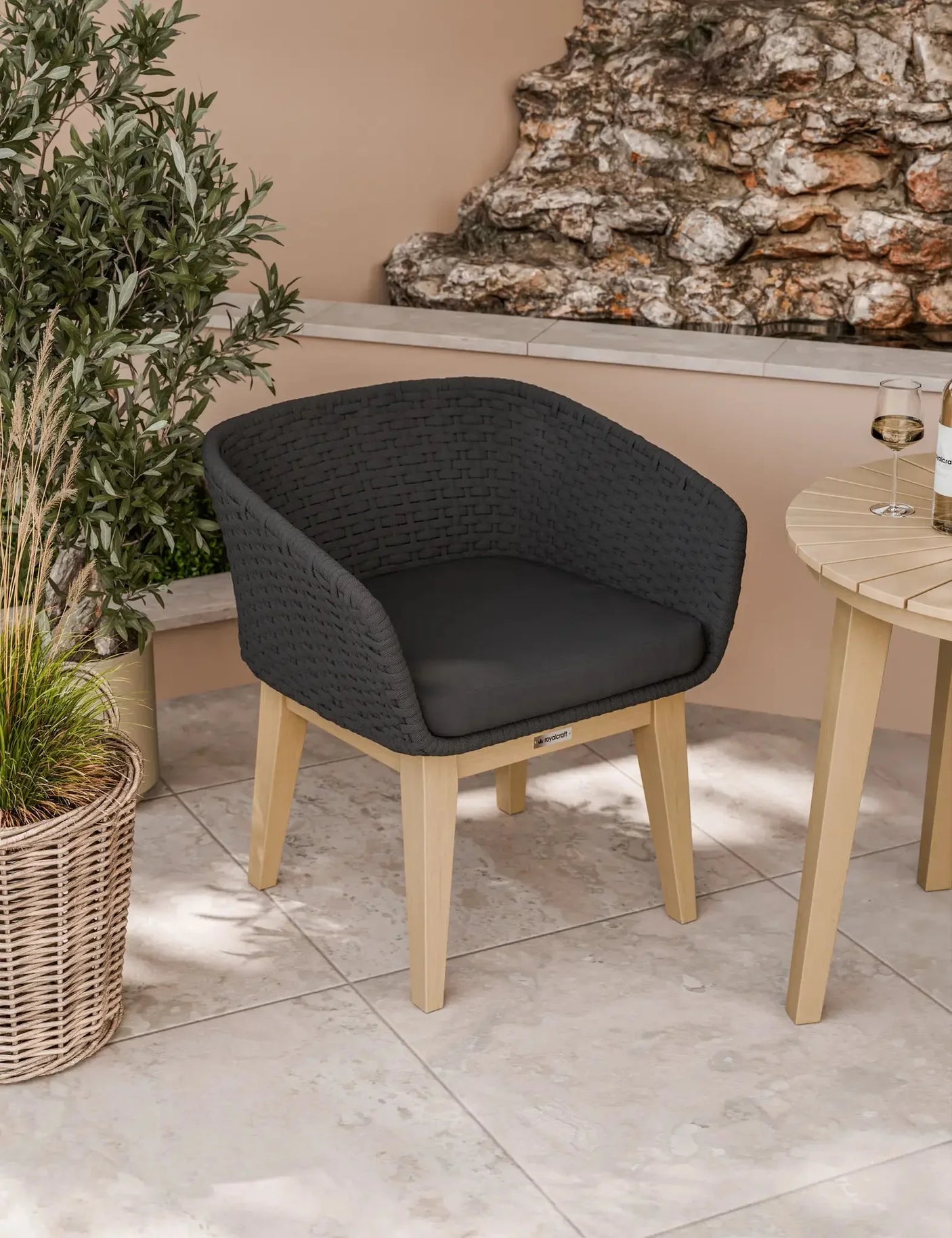 Outdoor dining chair with black woven seat and light wood legs on tiled patio