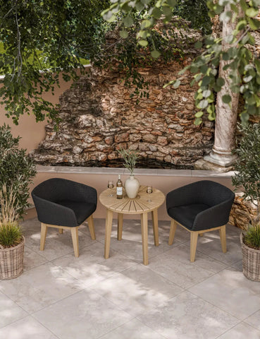 Outdoor bistro set with round wooden table and two black rattan chairs on tiled patio