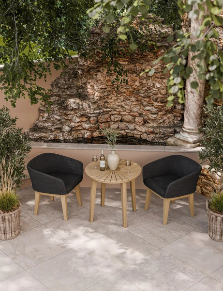 Outdoor bistro set with round wooden table and two black rattan chairs on tiled patio