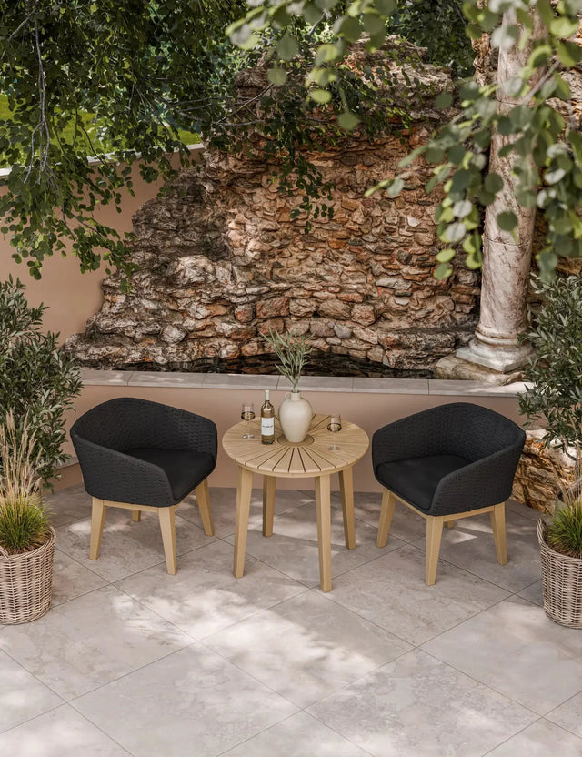 Outdoor bistro set with round wooden table and two black rattan chairs on tiled patio