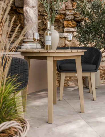 Beige outdoor dining table with wine bottle and glasses, paired with black woven chairs