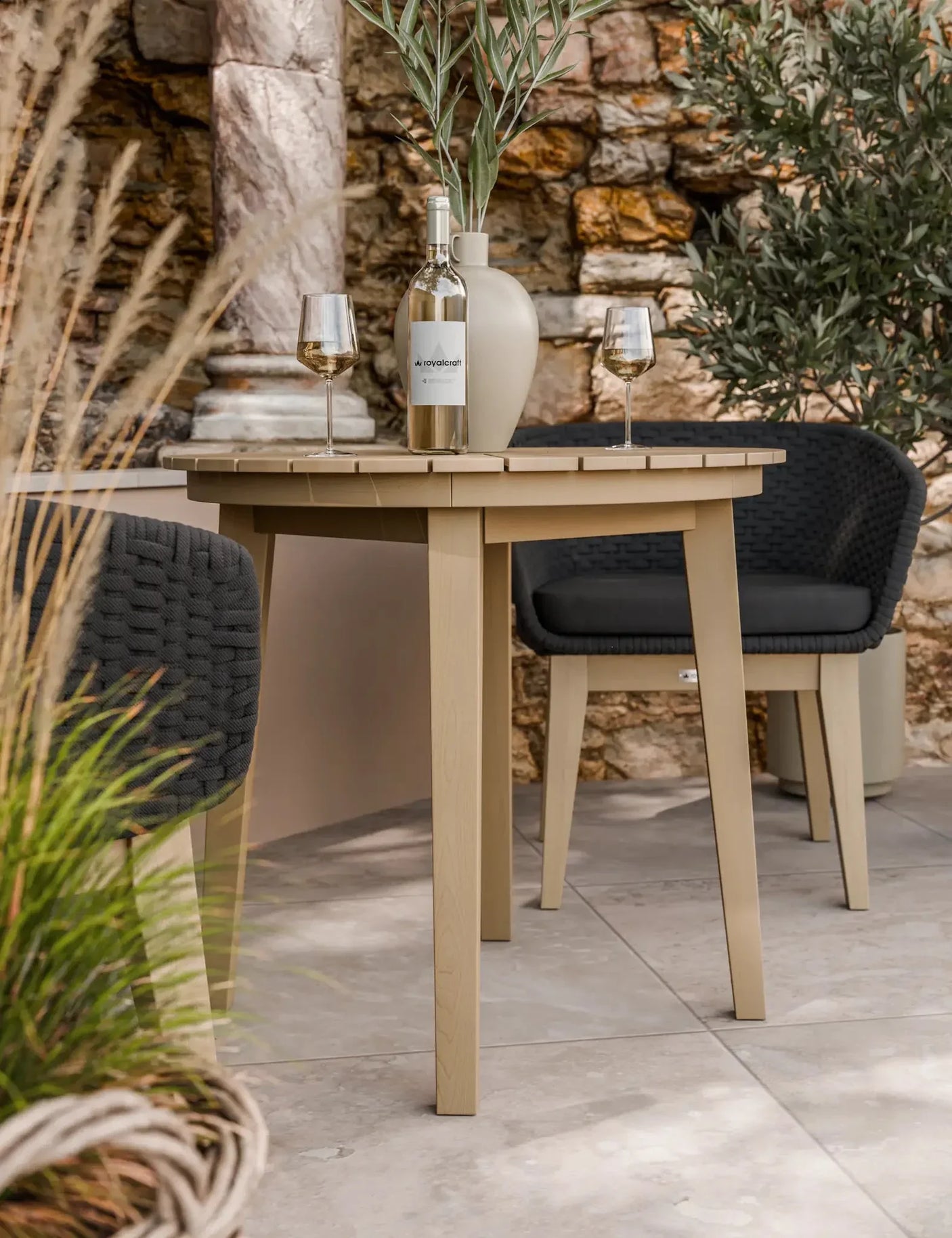 Beige outdoor dining table with wine bottle and glasses, paired with black woven chairs