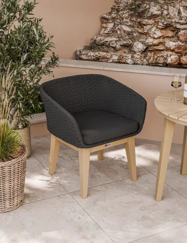 Black rattan outdoor dining chair with wooden legs on patio beside round table