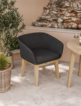 Black rattan outdoor dining chair with wooden legs on patio beside round table