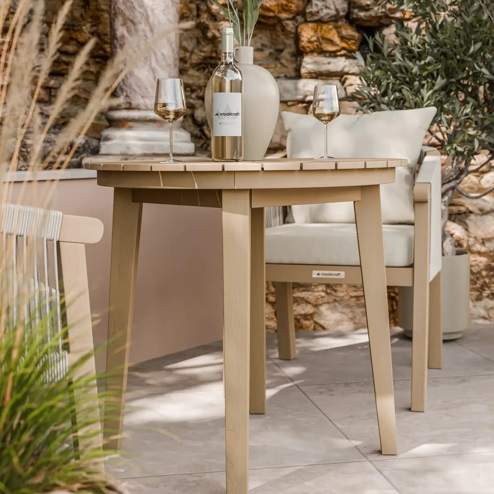 Light wood outdoor dining table with wine glasses and vase, patio stone backdrop