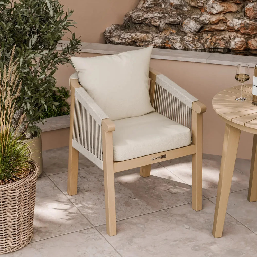 Beige outdoor dining chair with rope sides and cream cushions on tiled patio