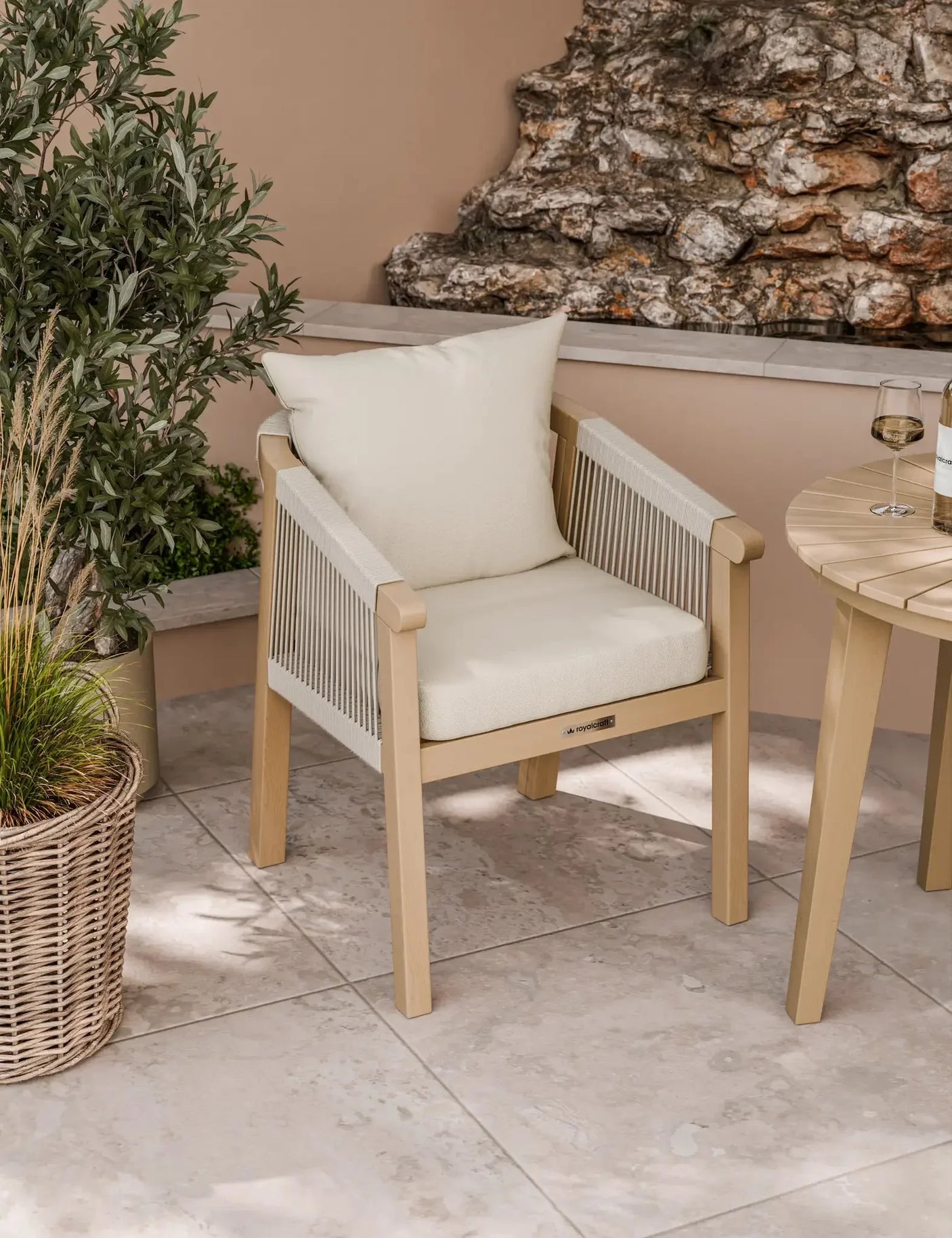 Beige outdoor dining chair with rope sides and cream cushions on tiled patio
