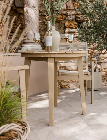 Outdoor wooden dining table and chair set with wine bottle, glasses, and vase on patio