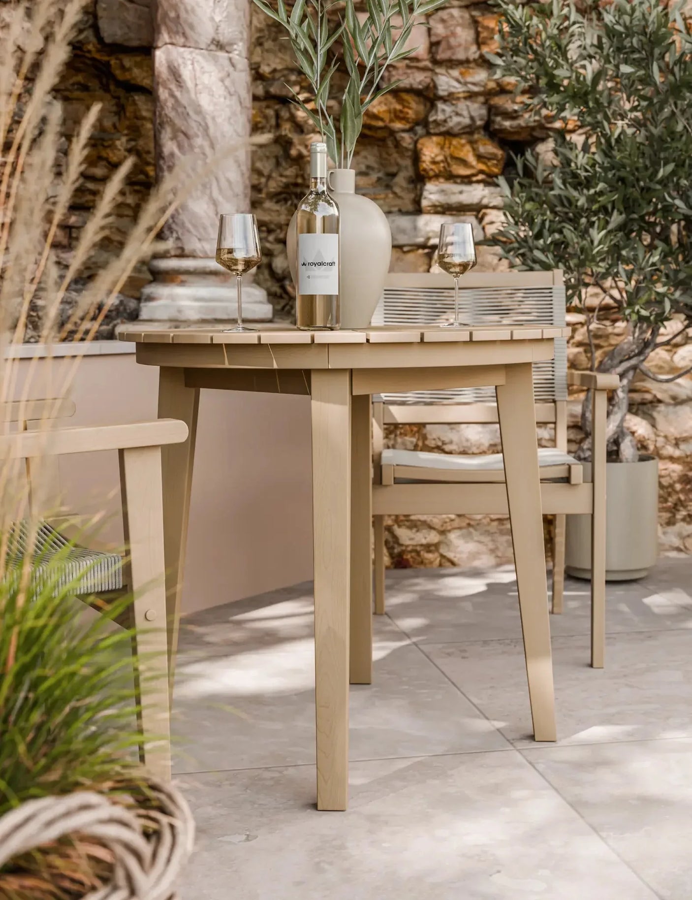 Outdoor wooden dining table and chair set with wine bottle, glasses, and vase on patio
