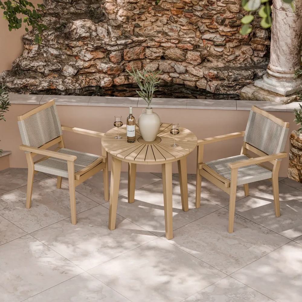 Outdoor bistro set with wooden table and two rope chairs on stone patio by a rock wall