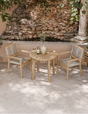 Outdoor bistro set with wooden table and two rope chairs on stone patio by a rock wall