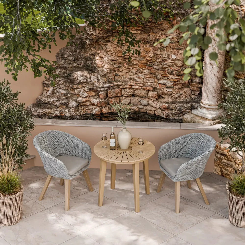 Outdoor bistro set with round wooden table and two grey rattan chairs on patio tiles