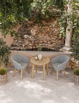 Outdoor bistro set with round wooden table and two grey rattan chairs on patio tiles