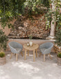 Outdoor bistro set with round wooden table and two grey rattan chairs on patio tiles