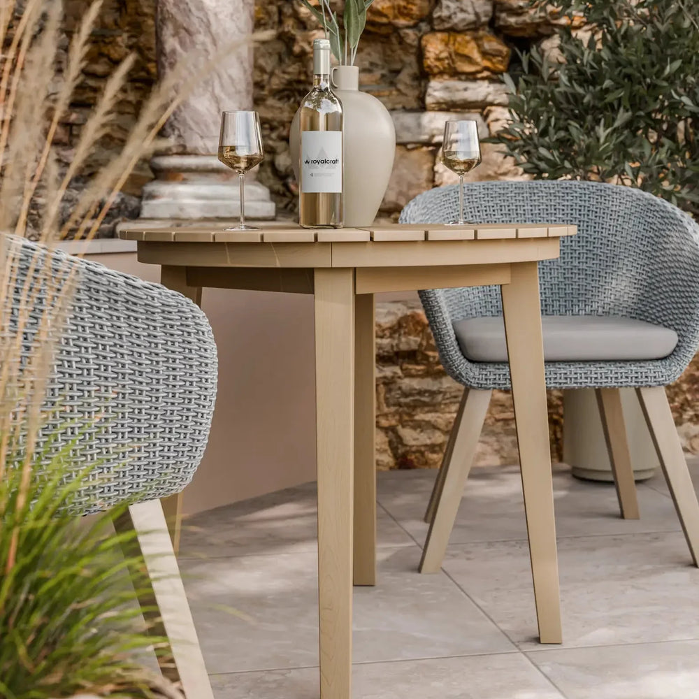 Outdoor rattan dining chairs and beige table set with wine and vase on stone patio