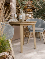 Outdoor rattan dining chairs and beige table set with wine and vase on stone patio