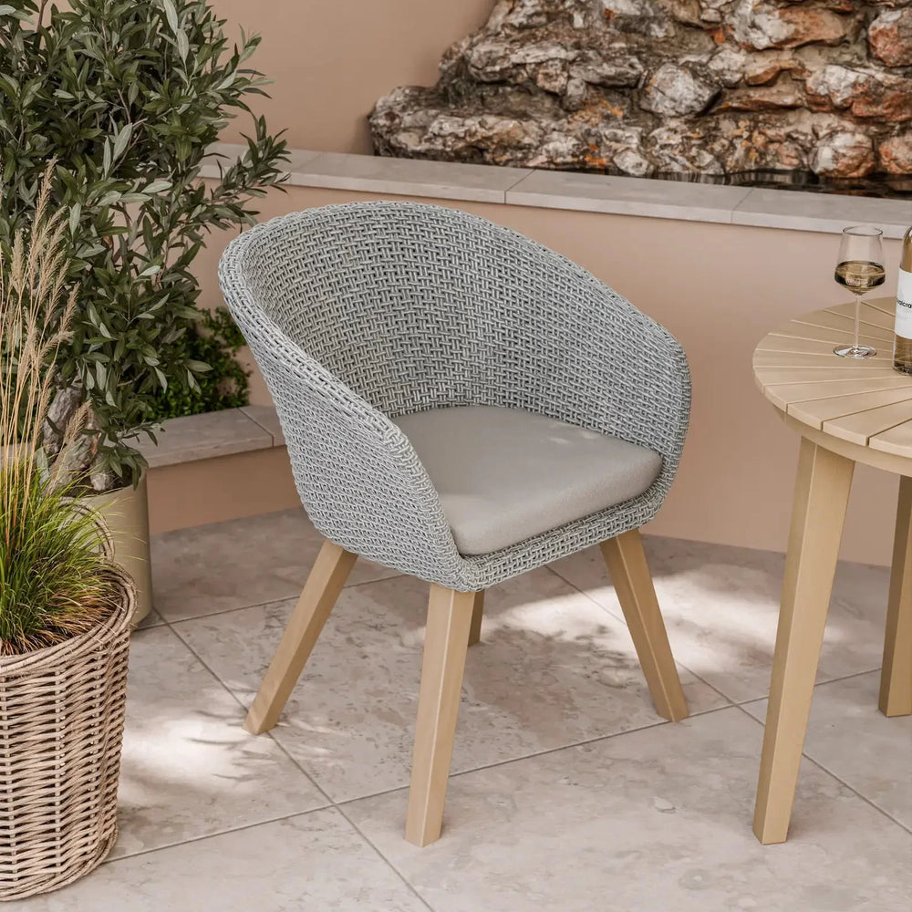 Grey rattan garden chair with cushion and wooden legs beside outdoor table
