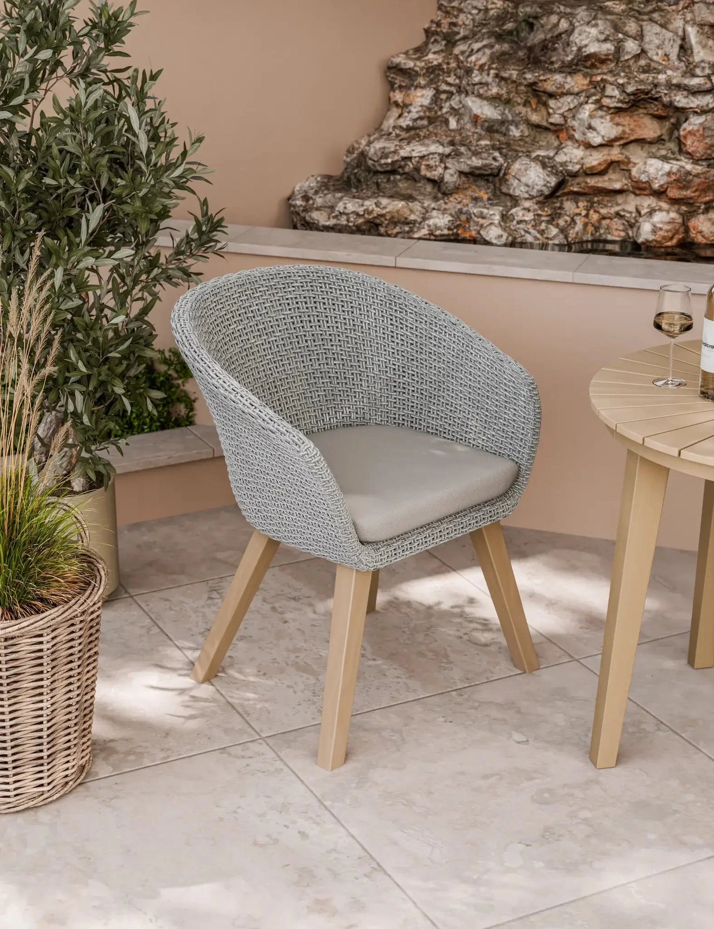 Grey rattan garden chair with cushion and wooden legs beside outdoor table