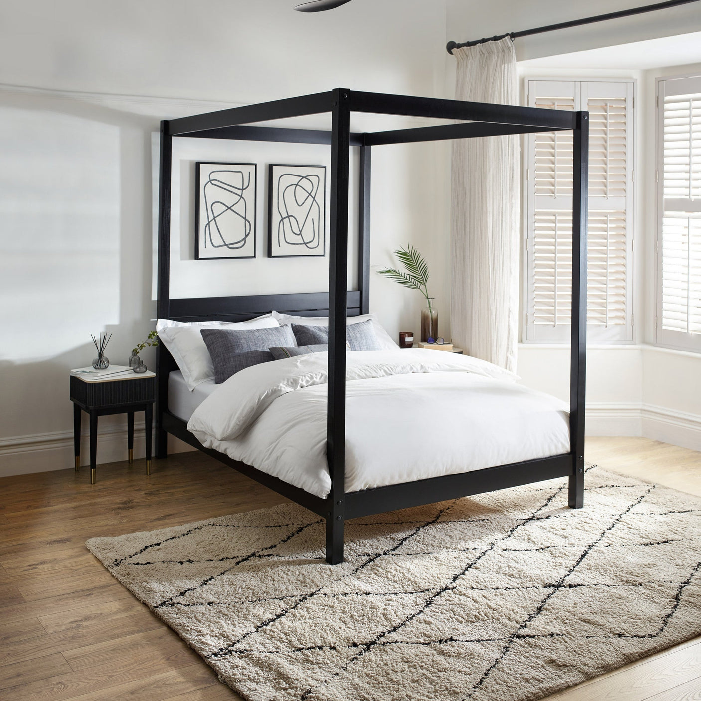 Black wooden canopy bed with white bedding, grey pillows, light wood floor, textured rug, and modern wall art