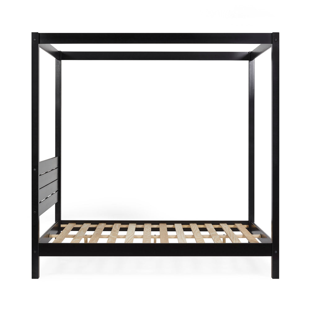 Close-up on black wooden canopy bed post with blurred modern wall art in the background