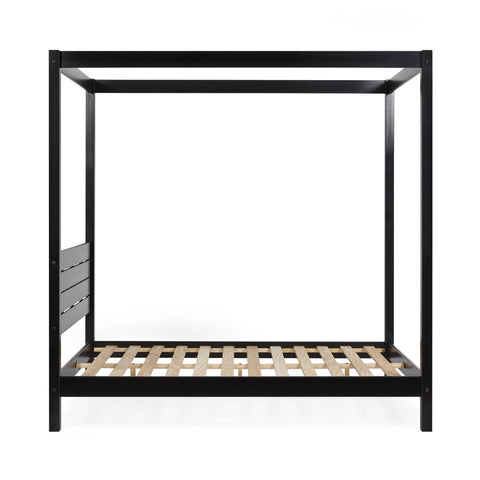 Close-up on black wooden canopy bed post with blurred modern wall art in the background