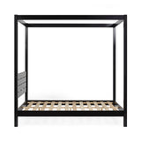 Close-up on black wooden canopy bed post with blurred modern wall art in the background
