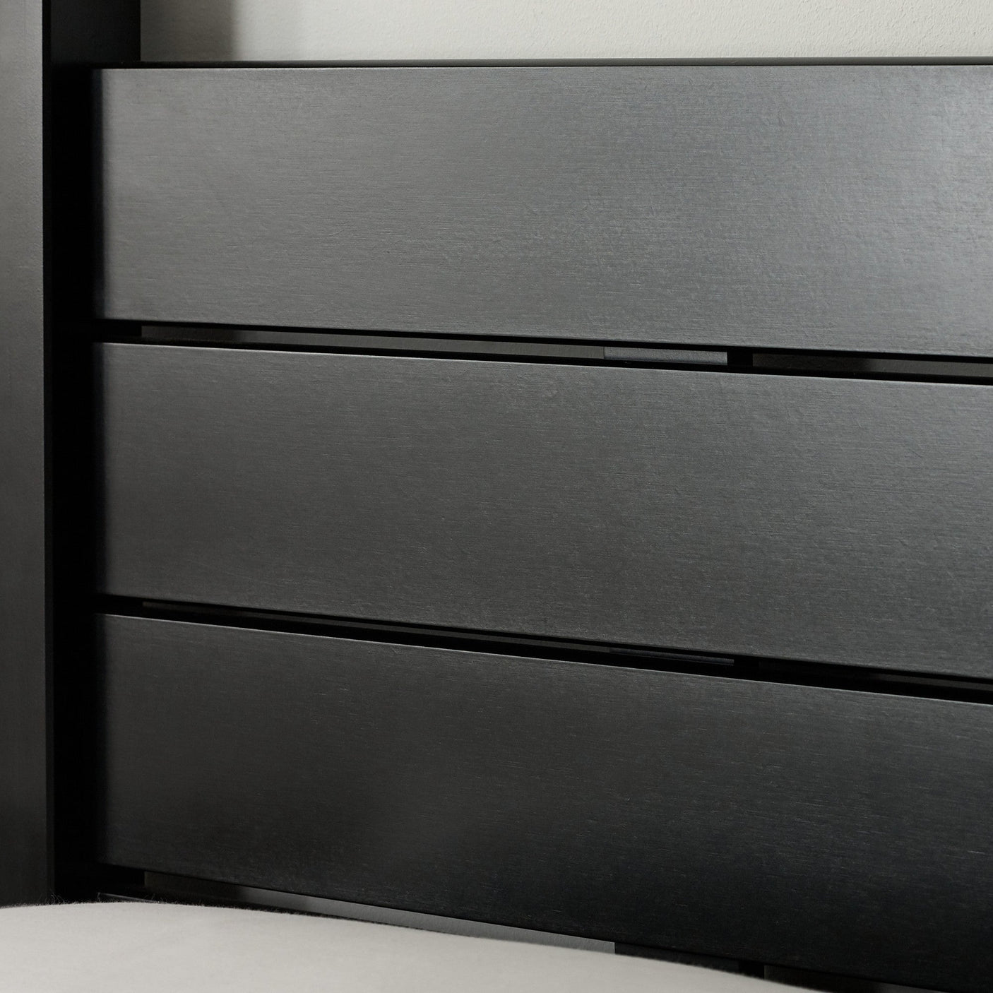 Close-up of black wooden canopy bed footboard with metal bolts and smooth finish, on a textured rug