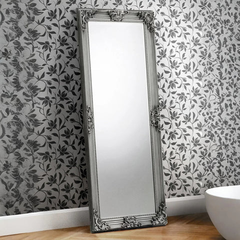Rococo full length mirror with ornate silver frame leaning against floral wallpapered wall
