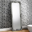 Rococo full length mirror with ornate silver frame leaning against floral wallpapered wall