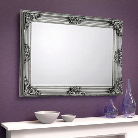 Rococo wall mirror with ornate silver frame above white mantel against purple wall