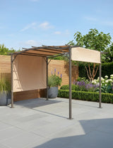 Metal garden pergola with beige fabric canopy on stone patio, surrounded by plants and flowers