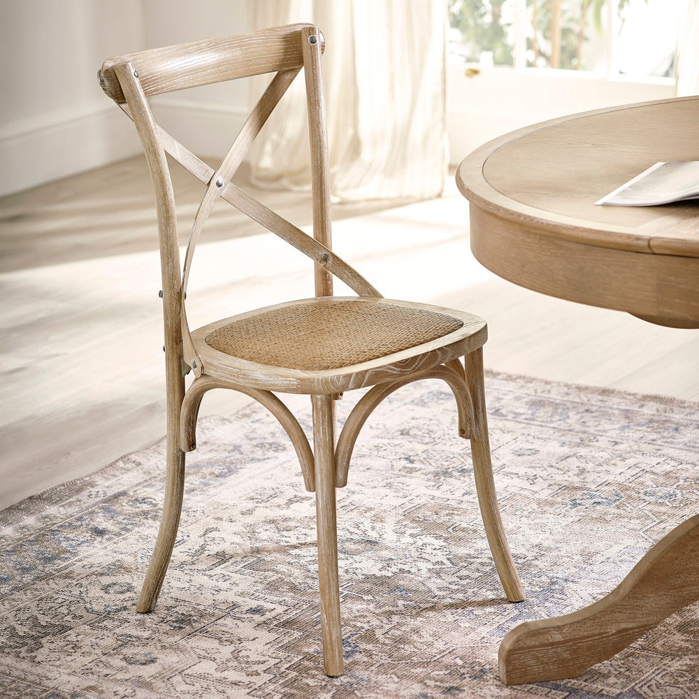 Light wooden dining chair with cane seat angled in bright room near round wooden table